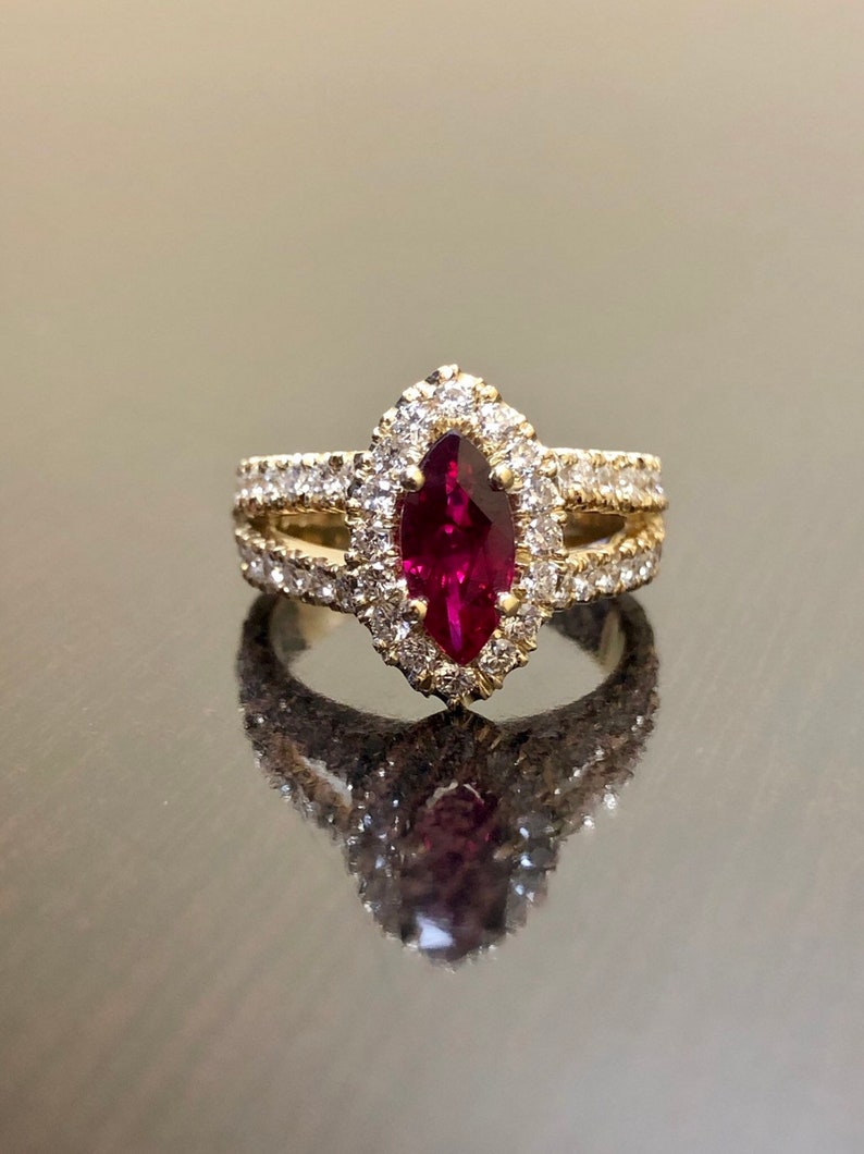 May include: A gold ring with a large, red, marquise-shaped gemstone surrounded by smaller, white gemstones.