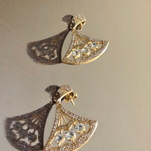 May include: A pair of gold earrings with a fan-shaped design and clear cubic zirconia stones.