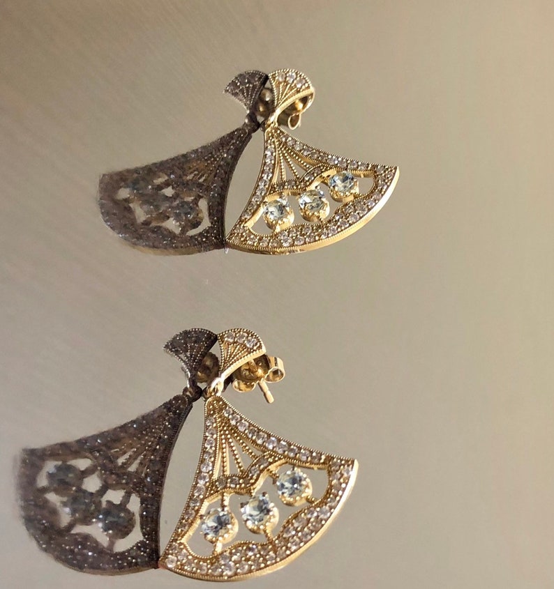 May include: A pair of gold earrings with a fan-shaped design and clear cubic zirconia stones.