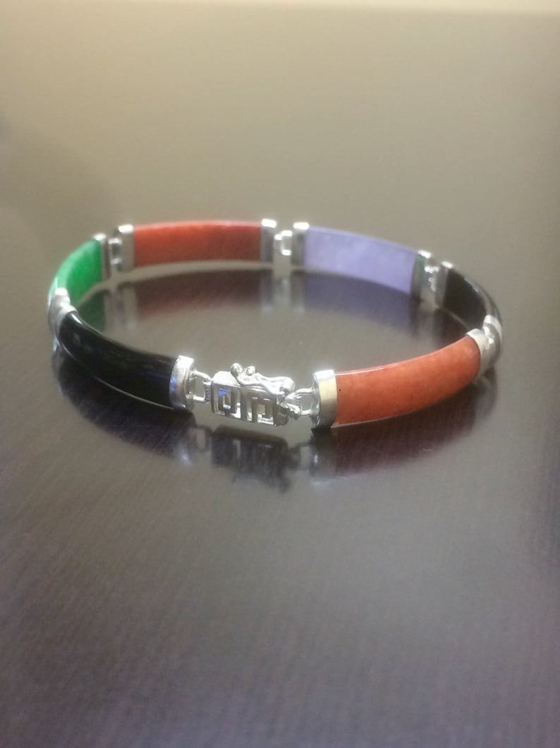May include: A multi-colored jade bracelet with a silver clasp. The bracelet is made of green, orange, black, and purple jade.