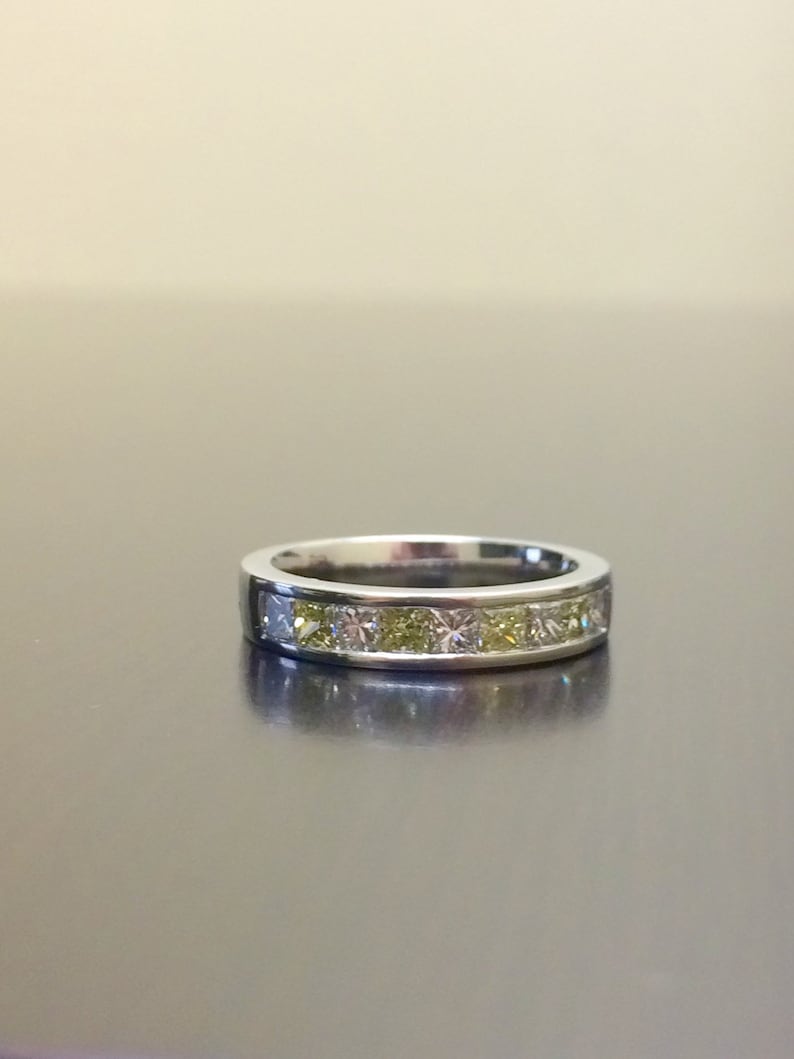 May include: A silver band ring with a row of small, square-shaped diamonds. The diamonds are a mix of clear and yellow.