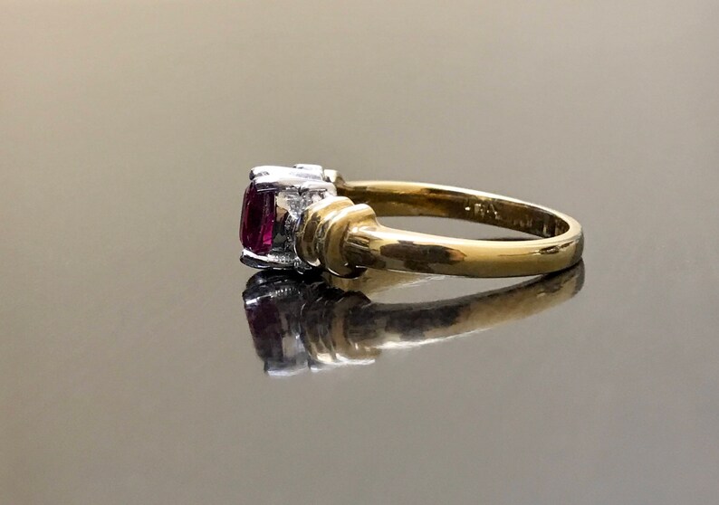 May include: A gold ring with a pink gemstone and two smaller white gemstones. The ring is set in a twisted band.