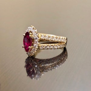 May include: A gold ring with a large, pear-shaped ruby surrounded by a halo of smaller diamonds. The ring has a split shank with a row of diamonds on each side.
