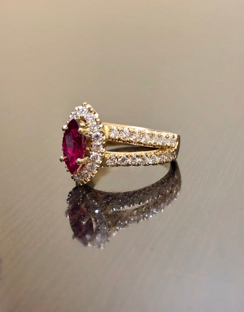 May include: A gold ring with a large, pear-shaped ruby surrounded by a halo of smaller diamonds. The ring has a split shank with a row of diamonds on each side.