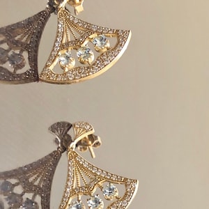 May include: A pair of gold earrings with a fan-shaped design and clear cubic zirconia stones.