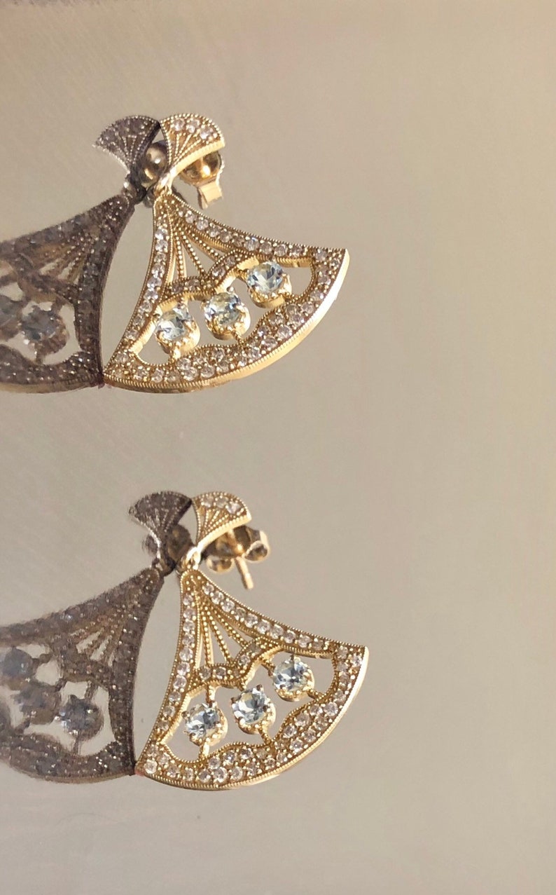 May include: A pair of gold earrings with a fan-shaped design and clear cubic zirconia stones.