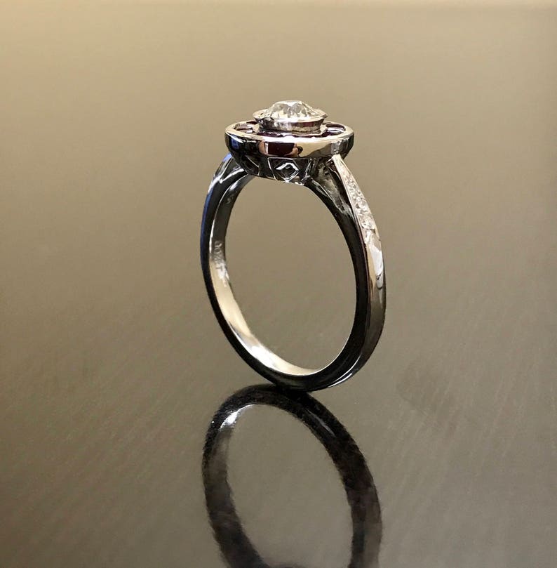 May include: A silver ring with a round, clear center stone surrounded by a halo of red stones. The band is set with small, clear stones.