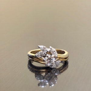 May include: A gold and white diamond engagement ring with a round center stone and a leaf design. The ring is set on a black background.