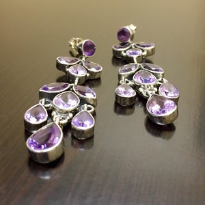 May include: A pair of dangle earrings with multiple amethyst gemstones in a cascading design. The earrings are made of silver and have a polished finish.