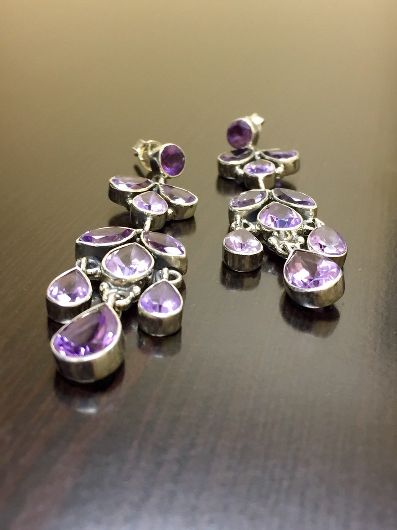 May include: A pair of dangle earrings with multiple amethyst gemstones in a cascading design. The earrings are made of silver and have a polished finish.