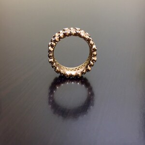 Pu&ograve; includere: Un anello a fascia d'oro con una fila di piccoli diamanti incastonati nel metallo. L'anello &egrave; su una superficie scura.