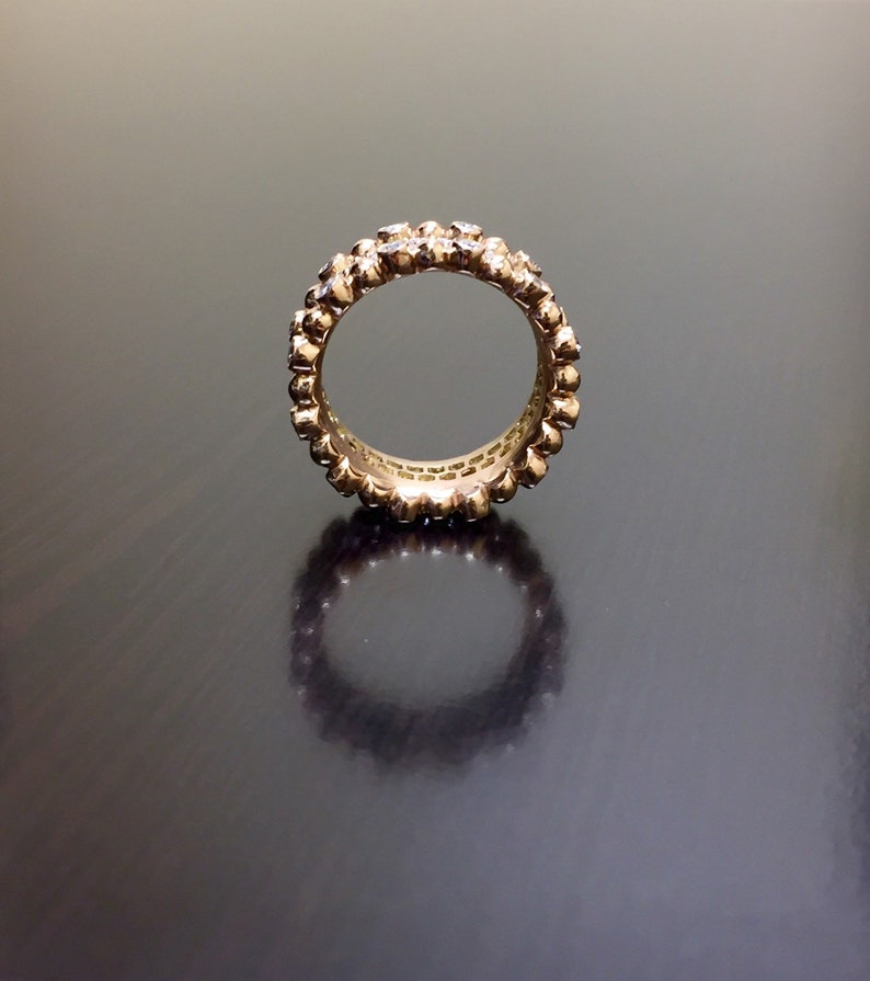 Pu&ograve; includere: Un anello a fascia d'oro con una fila di piccoli diamanti incastonati nel metallo. L'anello &egrave; su una superficie scura.