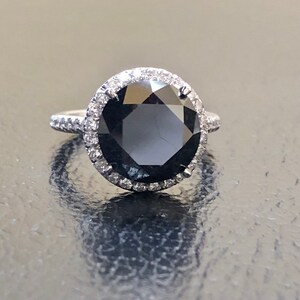 May include: A black diamond engagement ring with a halo of smaller diamonds set in white gold.