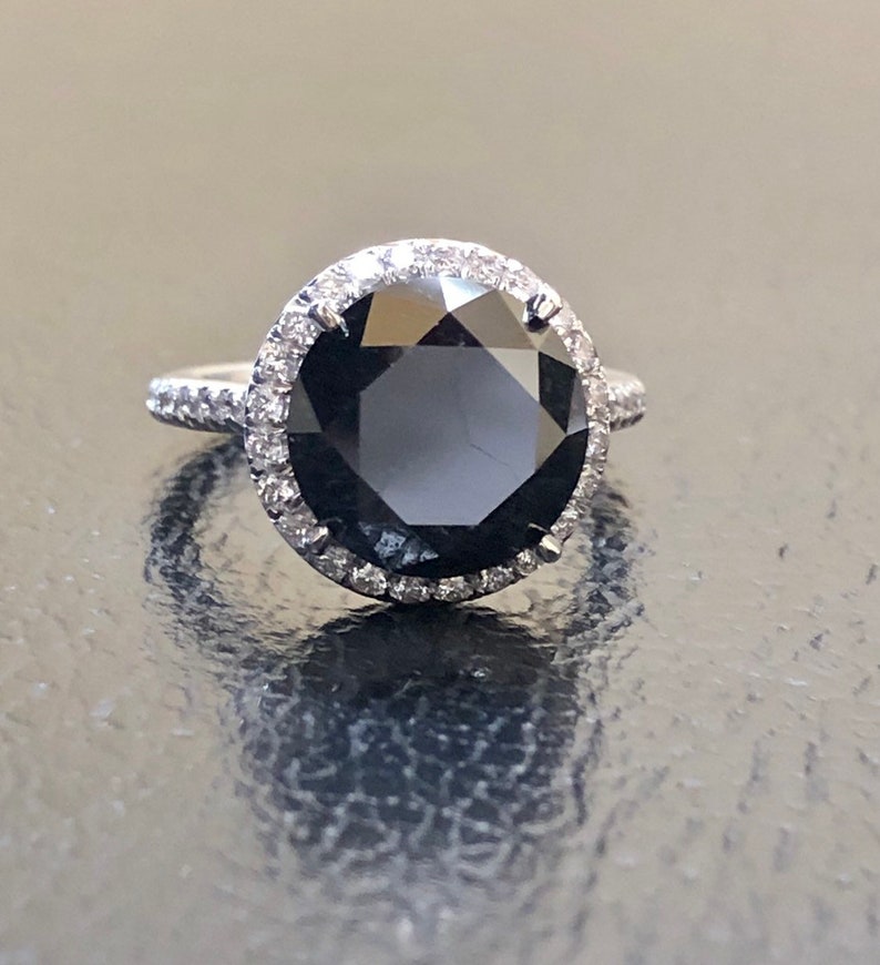 May include: A black diamond engagement ring with a halo of smaller diamonds set in white gold.