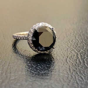 May include: A black diamond engagement ring with a halo of smaller diamonds set in white gold.