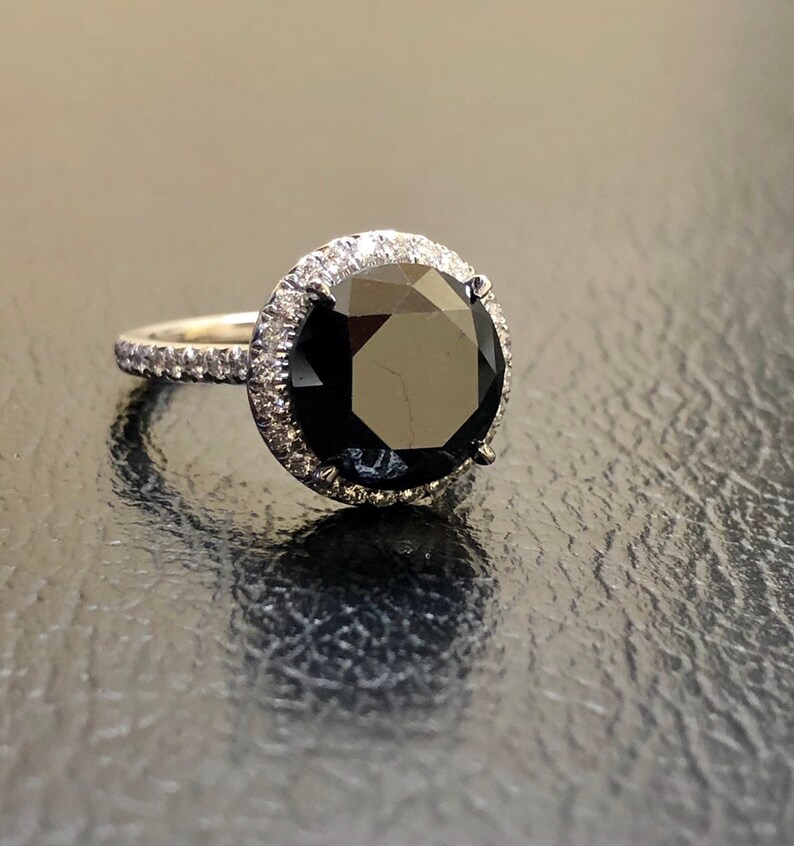 May include: A black diamond engagement ring with a halo of smaller diamonds set in white gold.