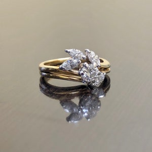 May include: A gold and white diamond engagement ring with a floral design. The ring features a round center stone surrounded by smaller diamonds in a leaf-like pattern.