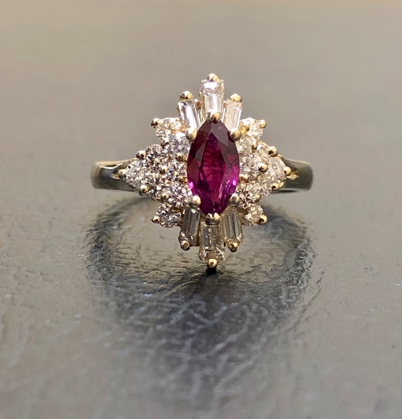 Op de afbeelding: Een gouden ring met een grote, marquise-vormige robijn omringd door een cluster van kleinere diamanten.