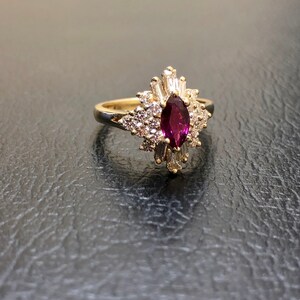 May include: A gold ring featuring a marquise-shaped ruby surrounded by a halo of smaller diamonds.