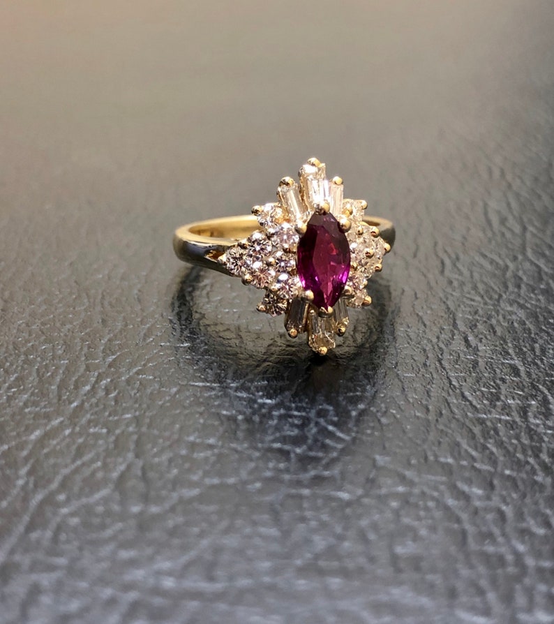 May include: A gold ring featuring a marquise-shaped ruby surrounded by a halo of smaller diamonds.