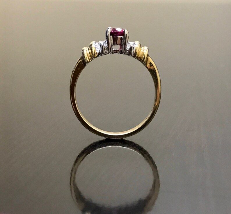 May include: A gold and silver ring with a red gemstone and smaller white gemstones.