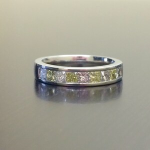 May include: A silver band ring with a row of small square-shaped diamonds. The diamonds are a mix of clear and yellow.