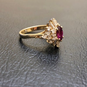 May include: A gold ring featuring a large oval ruby surrounded by smaller diamonds. The ring is set in a delicate, fan-shaped design.