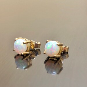 May include: A pair of gold stud earrings with white opal gemstones. The earrings have a simple, classic design.