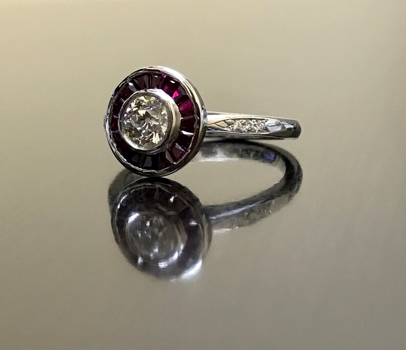 May include: A silver ring with a round center stone surrounded by a halo of red rubies. The band is set with smaller diamonds.