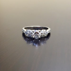 May include: A silver ring with three round diamonds. The centre diamond is larger than the two diamonds on either side.