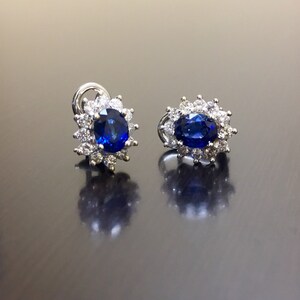 May include: A pair of silver earrings with a blue oval sapphire surrounded by a halo of smaller diamonds.