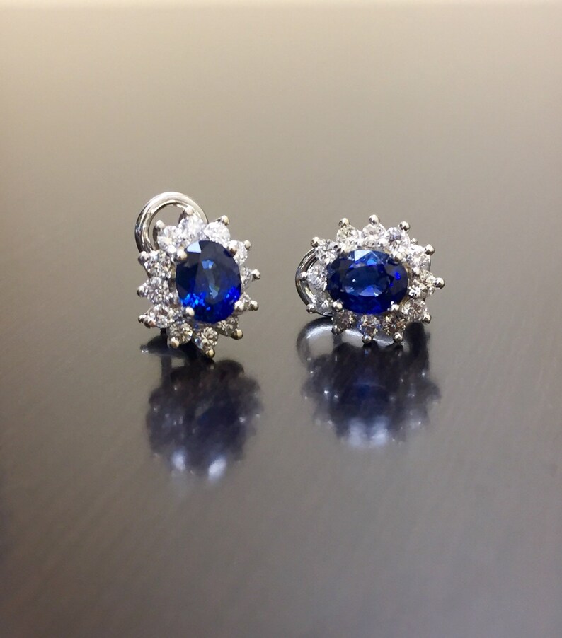 May include: A pair of silver earrings with a blue oval sapphire surrounded by a halo of smaller diamonds.