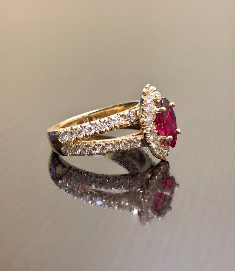 May include: A gold ring with a red gemstone surrounded by smaller diamonds. The ring has a split shank with diamonds on both sides.