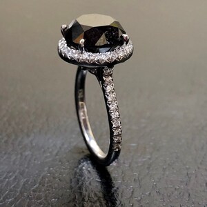 May include: A black diamond engagement ring with a halo of smaller diamonds set in a white gold band.