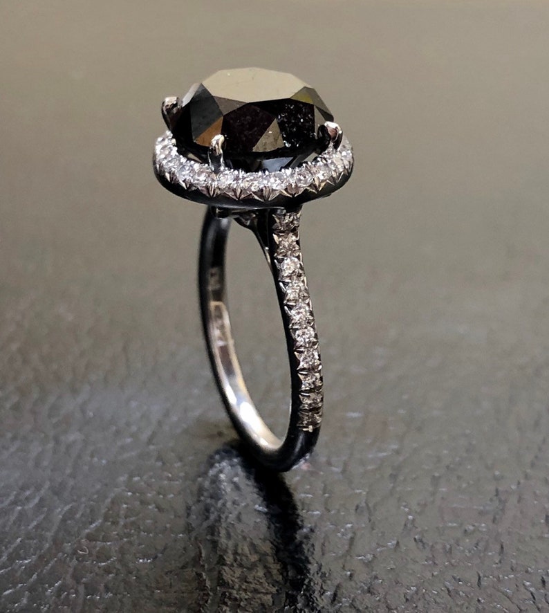 May include: A black diamond engagement ring with a halo of smaller diamonds set in a white gold band.