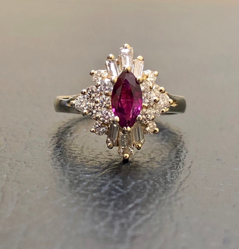 May include: A gold ring featuring a large, marquise-shaped ruby surrounded by a cluster of smaller diamonds.