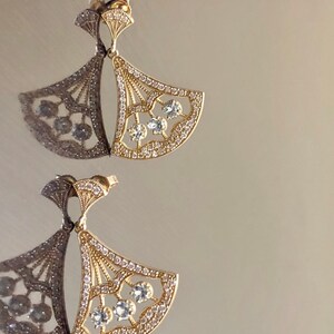 May include: A pair of gold earrings with a fan-shaped design. The earrings are adorned with clear crystals.