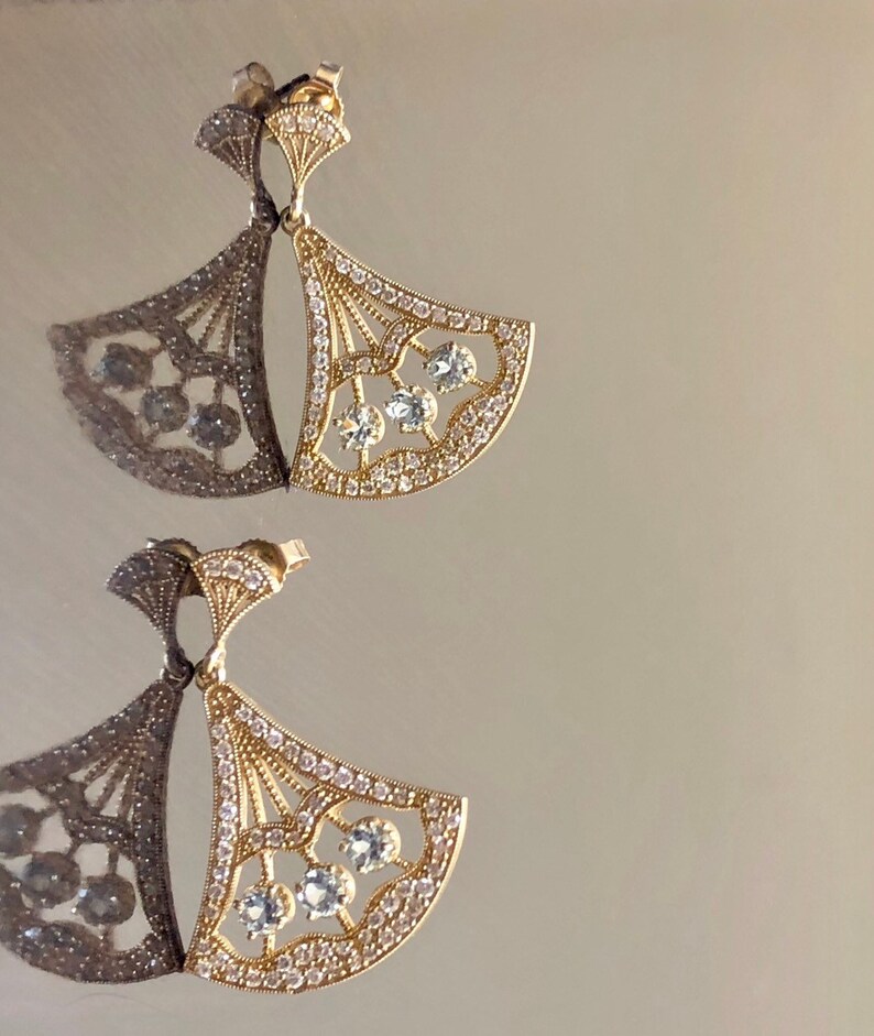 May include: A pair of gold earrings with a fan-shaped design. The earrings are adorned with clear crystals.