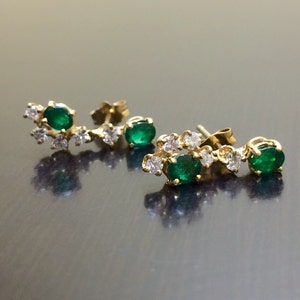 May include: A pair of gold earrings with emerald green gemstones and small diamonds. The earrings are designed in a curved shape with the gemstones set in a cluster.