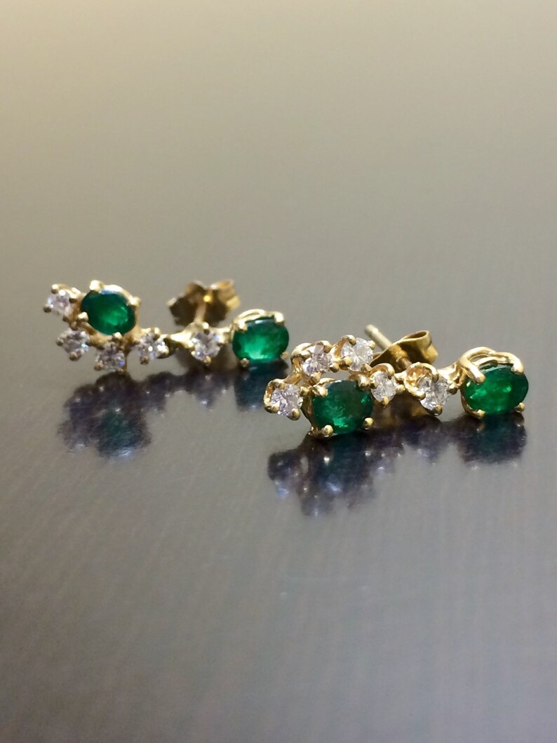 May include: A pair of gold earrings with emerald green gemstones and small diamonds. The earrings are designed in a curved shape with the gemstones set in a cluster.