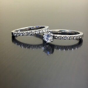 May include: A set of two silver wedding bands with a single round diamond on the larger band. Both bands are set with small diamonds.
