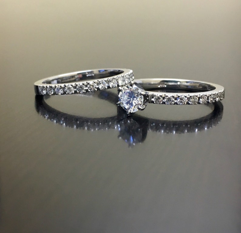 May include: A set of two silver wedding bands with a single round diamond on the larger band. Both bands are set with small diamonds.