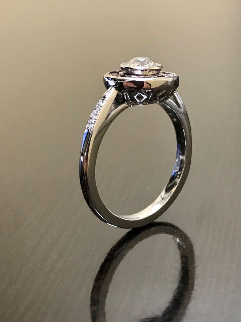 May include: A silver engagement ring with a round center diamond surrounded by a halo of smaller diamonds and a band of smaller diamonds. The halo is accented with red gemstones.