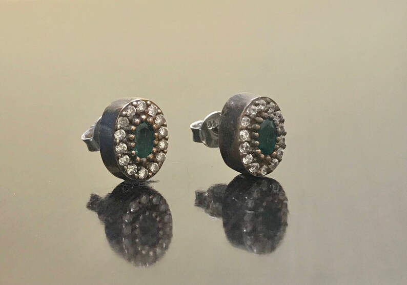 May include: A pair of silver earrings with a green oval stone surrounded by small white stones.