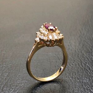 May include: A gold ring featuring a large, oval-shaped purple gemstone surrounded by smaller, clear gemstones.