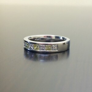 May include: A silver band ring with a row of clear and yellow square-shaped gemstones.