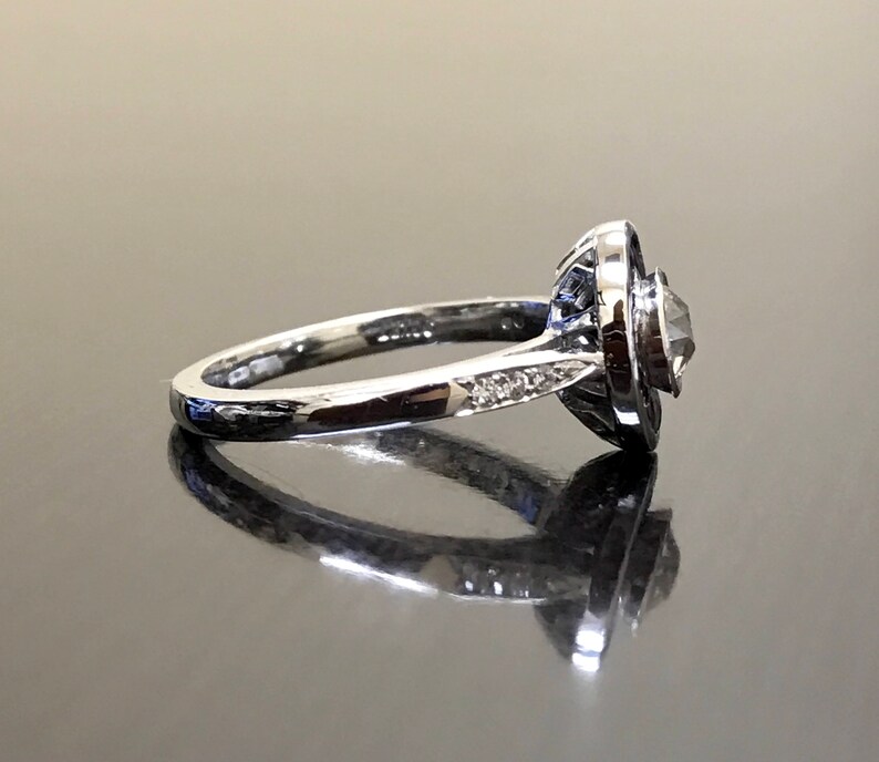 May include: A silver ring with a round, clear gemstone surrounded by a halo of smaller gemstones. The ring has a simple band.