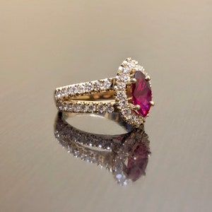May include: A gold ring with a large, marquise-shaped ruby surrounded by a halo of smaller diamonds. The ring has a double band with diamonds set in the metal.