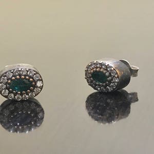 May include: A pair of silver earrings with a green oval stone surrounded by small white stones.