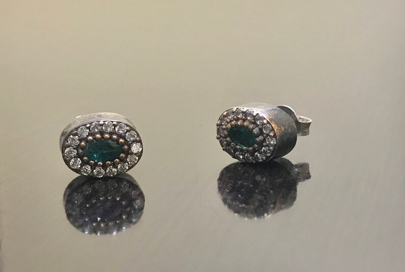May include: A pair of silver earrings with a green oval stone surrounded by small white stones.